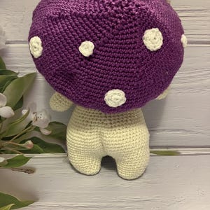 May include: A crocheted purple mushroom with white polka dots and a cream-colored body.