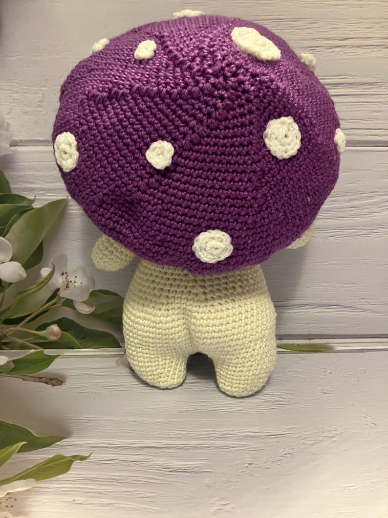 May include: A crocheted purple mushroom with white polka dots and a cream-colored body.