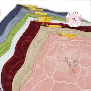 Puede incluir: Una pila de alfombras de oraci&oacute;n en varios colores, incluyendo rosa, beige, rojo, blanco, verde y azul. Las alfombras tienen una textura acolchada y un dise&ntilde;o decorativo. La alfombra superior tiene una borla dorada.