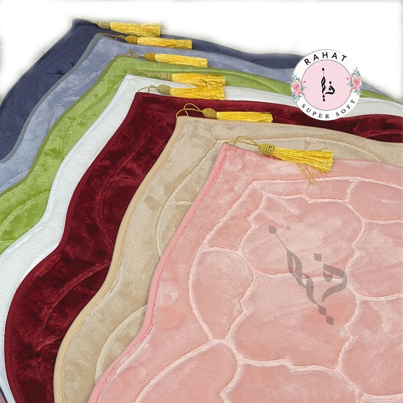 Puede incluir: Una pila de alfombras de oraci&oacute;n en varios colores, incluyendo rosa, beige, rojo, blanco, verde y azul. Las alfombras tienen una textura acolchada y un dise&ntilde;o decorativo. La alfombra superior tiene una borla dorada.