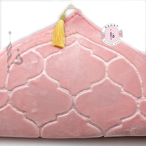 Puede incluir: Una alfombra de oraci&oacute;n rosa con un patr&oacute;n geom&eacute;trico y una borla dorada. La alfombra est&aacute; etiquetada como "Rahat Super Soft".