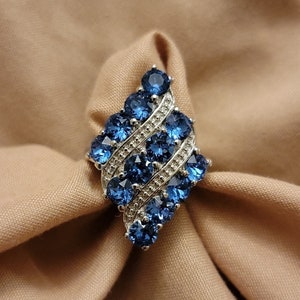 May include: A silver ring featuring a cluster of blue gemstones set in a diamond-shaped design.