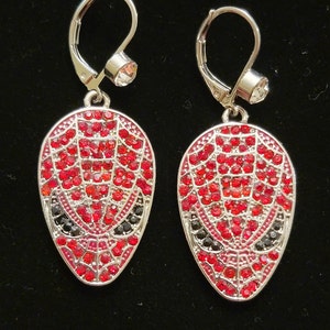 Peut inclure: Une paire de boucles d'oreilles pendantes argentées avec des embellissements en cristal rouge et noir en forme de masque de Spider-Man.