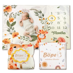 May include: A baby milestone blanket with a floral and giraffe design. The blanket has numbers 1-12 and the word "Months" printed on it. A wrapped blanket and box with the brand name "Böpe" are also visible.