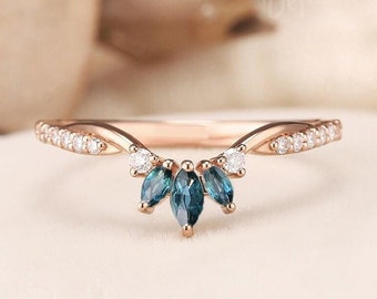 Puede incluir: Un anillo de oro rosa con una banda curva engastada con pequeñas piedras redondas transparentes en los laterales. El centro del anillo muestra tres piedras azules de talla marquesa dispuestas en abanico, con dos piedras transparentes a cada lado.