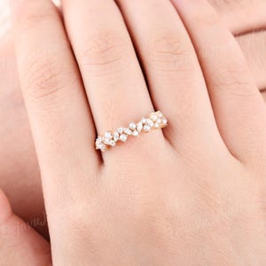 May include: A gold ring with a floral design, set with numerous small, clear gemstones. The ring is worn on a finger, highlighting its delicate and intricate details. The gemstones are arranged in a flowing, organic pattern.