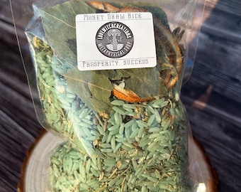 May include: A clear plastic bag filled with green-tinted rice, dried leaves, and herbs. A white label reads "MONEY DRAW RICE" and "PROSPERITY, SUCCESS" with a circular logo. The bag sits on a wooden slice.