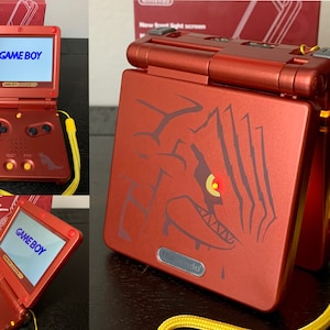 May include: A red Game Boy Advance SP handheld game console with a yellow wrist strap. The screen displays "GAME BOY". The console features a stylized graphic on the cover. The box is visible in the background.