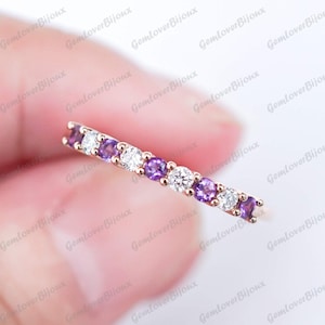 May include: A delicate ring featuring alternating round-cut amethyst and diamond gemstones set in a gold band. The ring showcases a repeating pattern of purple and clear stones, creating a sparkling and elegant design. The ring is a piece of jewelry.
