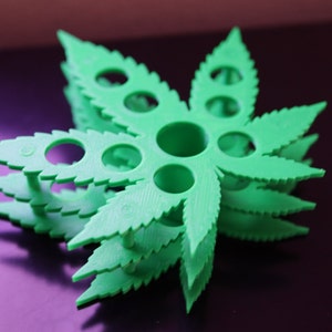 K&ouml;nnte beinhalten: Ein gr&uuml;ner, aus Kunststoff gefertigter Halter in Form eines Marihuana-Blattes mit mehreren L&ouml;chern zum Verstauen von Gegenst&auml;nden. Der Halter ist &uuml;bereinander gestapelt und erzeugt so einen 3D-Effekt.