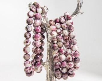May include: A set of five bracelets made of pink and white speckled stone beads. The bracelets are displayed on a silver tree-shaped stand.