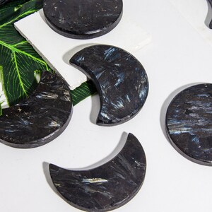 May include: Five black crescent moon-shaped stones with a shimmery blue and silver pattern. The stones are arranged on a white surface.
