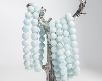 May include: Multiple strands of light blue aquamarine gemstone beads on a silver tree-shaped stand.