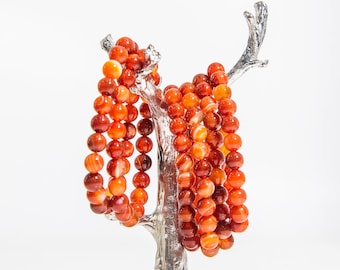 May include: A set of red carnelian gemstone bracelets, each with a different pattern of red and white stripes, displayed on a silver tree-shaped stand.