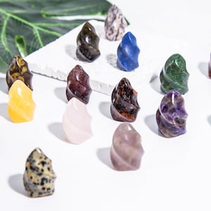 Puede incluir: Una colección de 11 pequeñas piedras pulidas en forma de espiral de varios colores, incluyendo rosa, amarillo, verde, azul, morado, marrón y negro. Las piedras están dispuestas sobre una superficie blanca.
