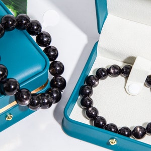 May include: Two teal velvet jewelry boxes with black gemstone beaded bracelets inside. The bracelets are made of round, shiny black beads.
