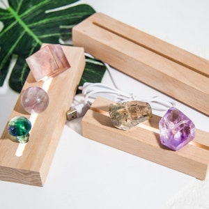 Op de afbeelding: Vier verschillende kristallen tentoongesteld op twee verlichte houten displays. De displays zijn gemaakt van natuurlijk hout en hebben een strak, modern ontwerp. De kristallen zijn een paarse amethist, een groene fluoriet, een heldere citrien en een roze amethist.