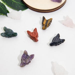Puede incluir: Una colección de ocho pequeñas figuritas talladas de cabeza de lobo hechas de varios tipos de piedras preciosas. Las figuritas son de color rojo, verde, negro, blanco, morado y marrón.
