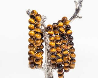 May include: Multiple strands of tiger's eye gemstone beads in a warm brown and gold color, displayed on a silver metal tree-shaped stand.