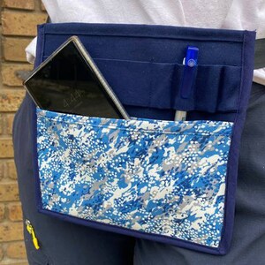 May include: A blue canvas utility belt with a camouflage fabric pocket. The belt has multiple pockets and loops for carrying tools and other items. A mobile phone and a pen are visible in the pockets.