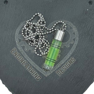 Peut inclure: Un collier avec un pendentif de niveau vert et argent sur une plaque en ardoise noire en forme de cœur avec les mots "Engineering Designs" gravés dessus.