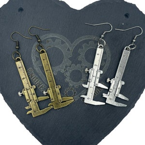 May include: A pair of earrings featuring a miniature caliper design. One pair is gold-toned, and the other pair is silver-toned.
