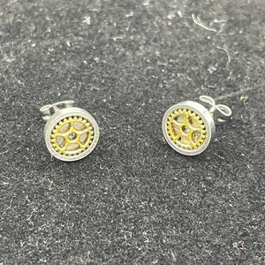May include: A pair of silver stud earrings with a gold gear design. The gears have a small clear stone in the centre.