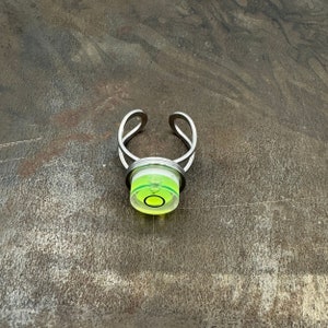 May include: A silver ring with a green and white spirit level bubble in the centre.