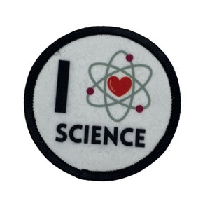 May include: A white round patch with black trim. The patch has a black "I" followed by a red heart inside a grey atom symbol. The text "SCIENCE" is printed in black below the atom symbol.