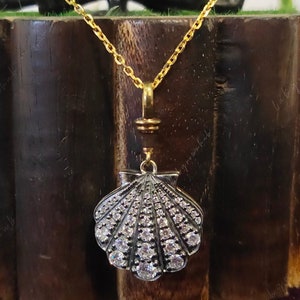 May include: A gold chain necklace with a silver seashell pendant. The seashell is encrusted with small, clear rhinestones.