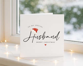 May include: A white square greeting card with black text that reads TO MY SPECIAL Husband MERRY CHRISTMAS. The design features a small red and white Santa hat resting on the letter H and a tiny red heart icon below the text.