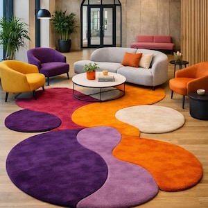 May include: A modern living room with a colorful rug and furniture. The rug features a unique, abstract design in shades of purple, orange, and beige. The room includes a gray sofa, armchairs in yellow, purple, and orange, and a round coffee table.