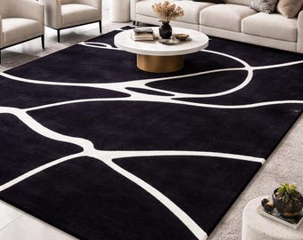 May include: A large, rectangular black rug with a white, abstract design. The rug is placed in a living room setting with neutral-toned furniture and decor. The rug's design features thick, curving white lines.