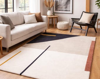 May include: A modern area rug with a geometric design in a living room setting. The rug features a cream-colored base with black, yellow, and rust-colored accents. The rug is rectangular and covers a portion of the hardwood floor.