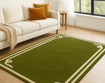 Puede incluir: Una alfombra verde rectangular con un borde crema y detalles decorativos en las esquinas. La alfombra está sobre un suelo de madera en un salón, con un sofá blanco y cojines visibles. Medidas en centímetros.