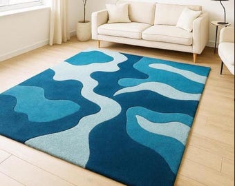 May include: A rectangular area rug with a blue and light blue abstract design. The rug features a dark blue base with lighter blue and white organic shapes. The rug is placed on a light wood floor in a living room setting.