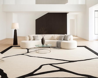 Puede incluir: Una alfombra rectangular grande con una base de color crema y líneas abstractas negras audaces que crean un patrón geométrico similar a ramas. La alfombra tiene un borde negro grueso que enmarca todo el diseño.