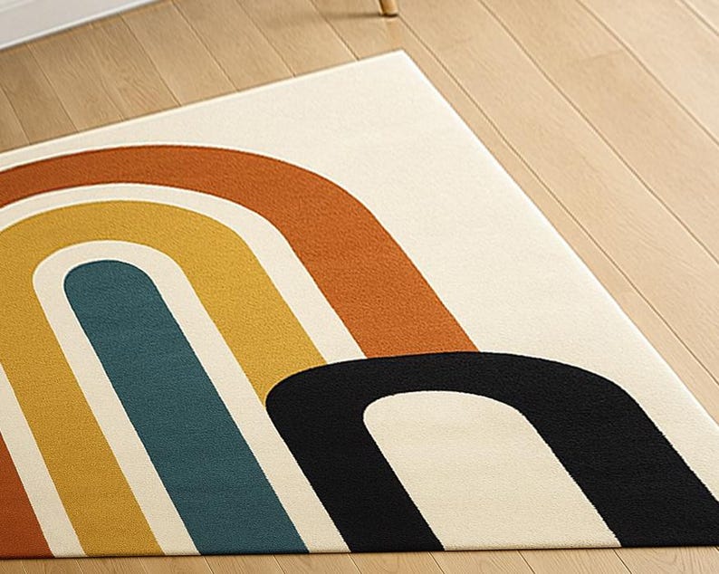 May include: A rectangular rug with a cream-colored background and a retro rainbow design. The rainbow arches are in shades of orange, yellow, teal, and black. The rug is placed on a light-colored wooden floor.