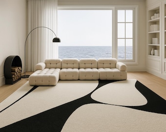 Puede incluir: Un salón moderno con un sofá seccional color crema y una gran alfombra con un diseño abstracto en blanco y negro. También hay una lámpara de pie arqueada negra y una chimenea negra con leña. La habitación tiene una gran ventana con vistas al mar.