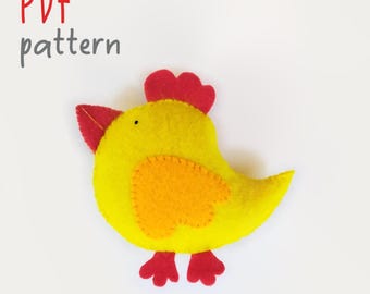 Könnte beinhalten: Ein gelbes Filzhuhn-Bastelobjekt mit rotem Kamm und Schnabel, einem orangefarbenen Flügel und roten Füßen. Der Text PDF pattern ist in Rot und Grau gehalten, der Text lapuchka in Grau. Das Huhn hat ein kleines schwarzes Auge und sichtbare Nähte.