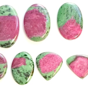 Könnte beinhalten: Sieben ovale und dreieckige Edelsteine mit grünen und rosa Mustern. Die Steine sind geschliffen und poliert für die Schmuckherstellung.
