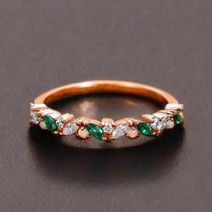 May include: Rose gold ring with alternating emerald green, white, and opal gemstones. The ring has a delicate design with small, marquise-cut stones set along the band. The gemstones are set in a repeating pattern.
