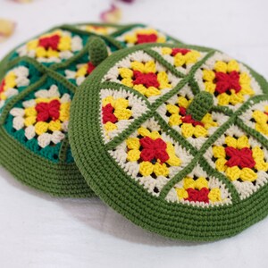 May include: Two green crocheted hats with a white and yellow geometric pattern and red flower accents.