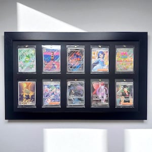 May include: A black framed display case holding ten collectible trading cards. Each card is encased in a clear protective sleeve. The cards feature colorful illustrations of various characters and designs.