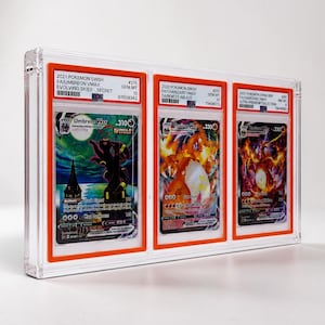 May include: A clear acrylic display case holding three graded Pok&eacute;mon trading cards. The cards feature Umbreon VMAX, Charizard VMAX, and Charizard VMAX. Each card is encased in a protective holder with grading information visible.