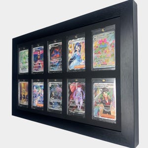 May include: A black framed display case holding ten trading cards. The cards are in individual protective sleeves. The cards feature colorful illustrations of various characters and creatures. The frame is rectangular and made of wood.