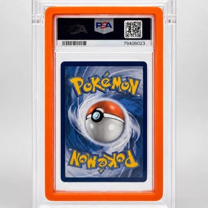 May include: A graded Pok&eacute;mon trading card in a clear plastic holder with an orange frame. The card shows the Pok&eacute;mon logo and a Pok&eacute; Ball design. The holder has a PSA label and a QR code.