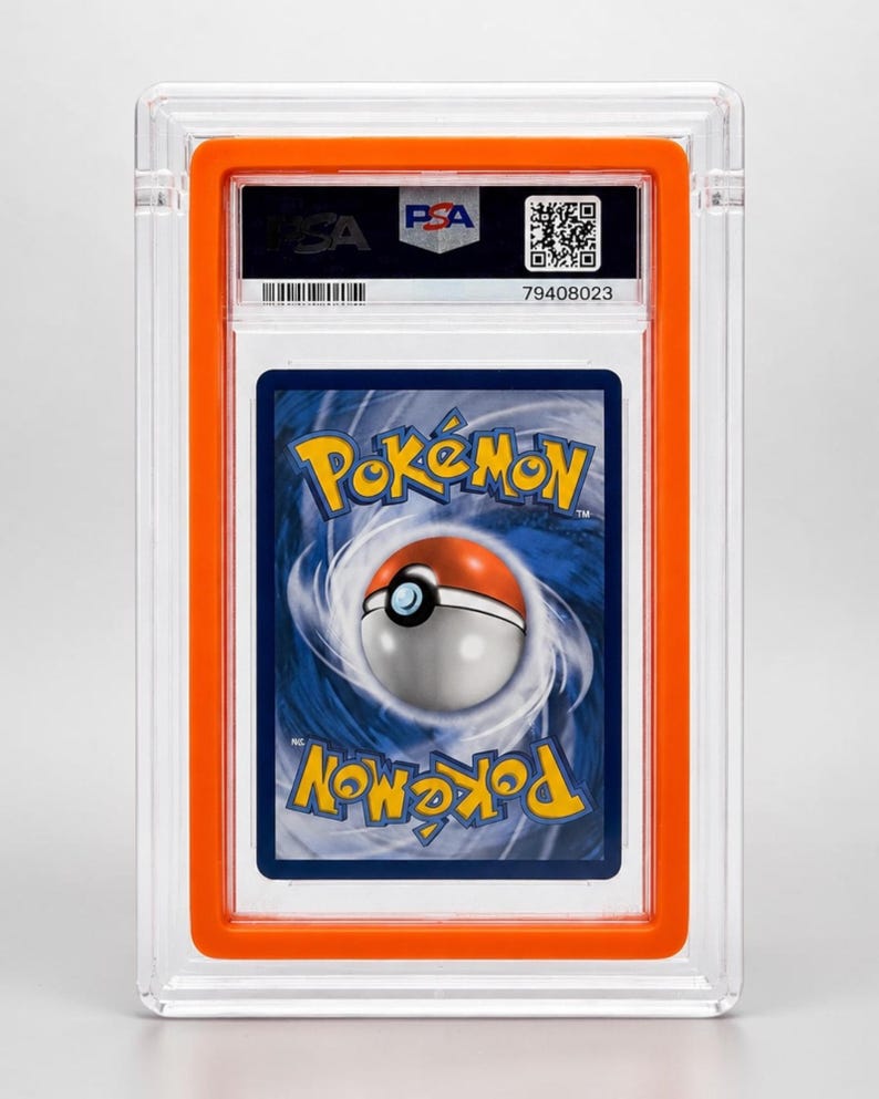 May include: A graded Pok&eacute;mon trading card in a clear plastic holder with an orange frame. The card shows the Pok&eacute;mon logo and a Pok&eacute; Ball design. The holder has a PSA label and a QR code.