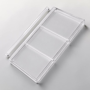 May include: A clear, rectangular plastic organizer with three compartments and a separate, cylindrical bar. The organizer is designed to hold small items and is made of transparent plastic.