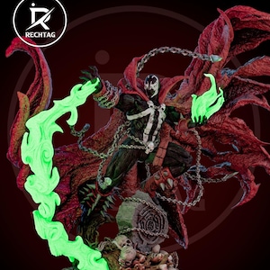 May include: A detailed action figure of Spawn, a comic book character, in a dynamic pose. The figure is predominantly black with white accents, a red cape, and chains. Green energy emanates from the figure's hands and a swirling trail. The base features skulls and a tombstone.
